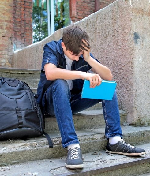 Crisis services image sad young white boy sitting on steps outside school