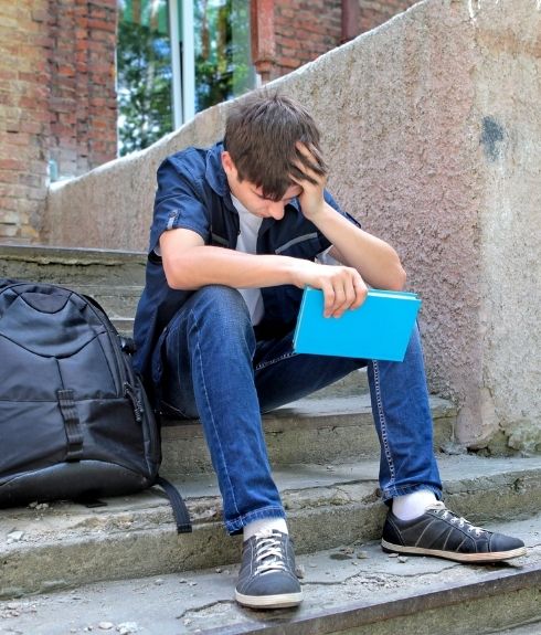 sad young white boy sitting on steps outside school