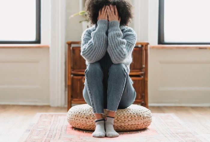 image of black woman sitting on the floor with her hands over her face indicating depression or sadness