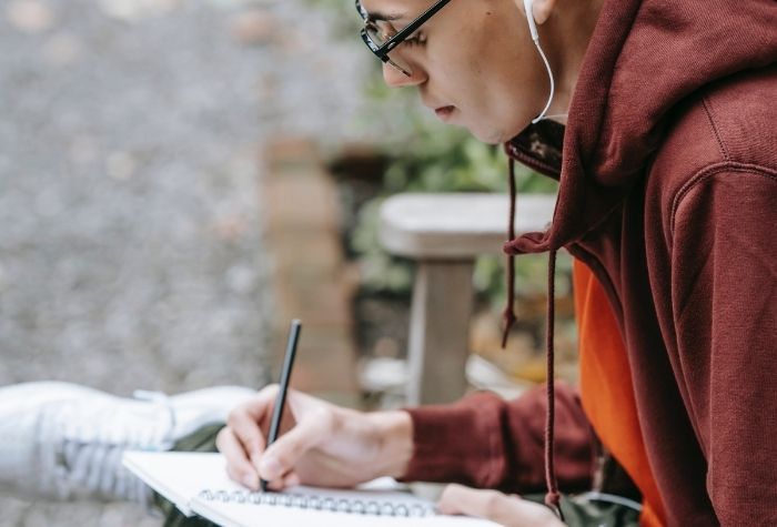 Young man writes in a notebook with headphones in his ears
