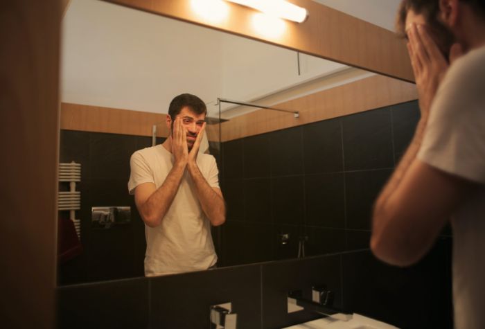 young man looking into mirror sad and contemplating