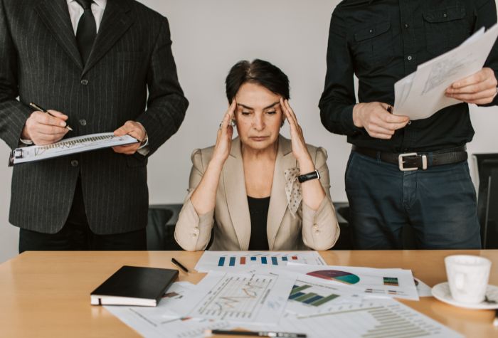 A woman sitting at a desk, surrounded by work and overwhelmed