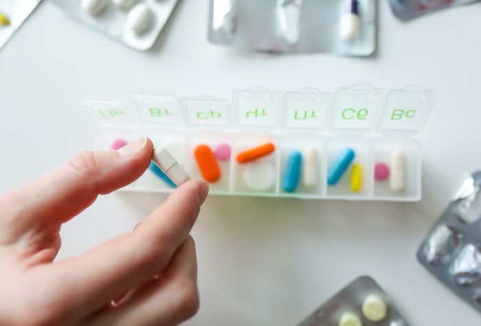 various colorful pills in a clear plastic weekly pill case against a white background